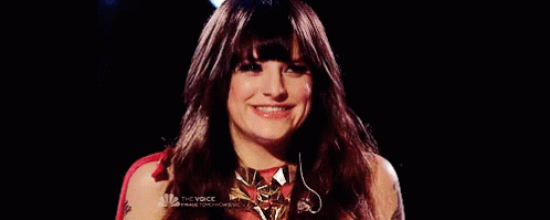 A Woman With Long Red Hair And Bangs Is Smiling In Front Of A Black Background . GIF