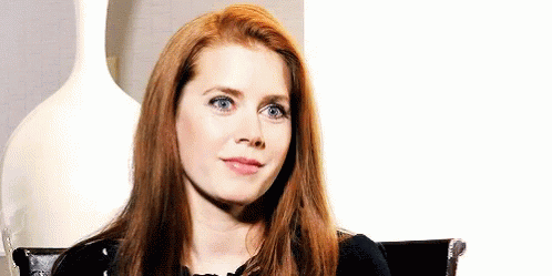 A Woman With Long Red Hair And Blue Eyes Is Sitting In A Chair . GIF