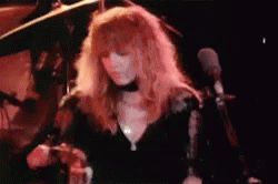 A Woman With Long Red Hair Is Singing Into A Microphone On Stage . GIF