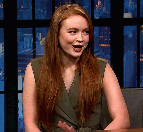 A Woman With Long Red Hair Is Sitting In Front Of A Window GIF