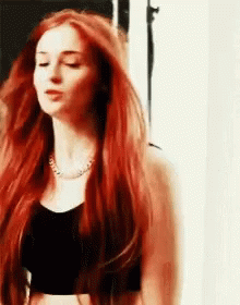 A Woman With Long Red Hair Is Wearing A Black Crop Top . GIF