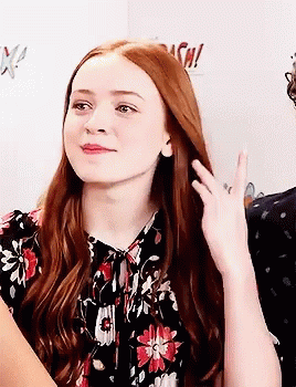 A Woman With Long Red Hair Is Wearing A Floral Shirt And Waving . GIF