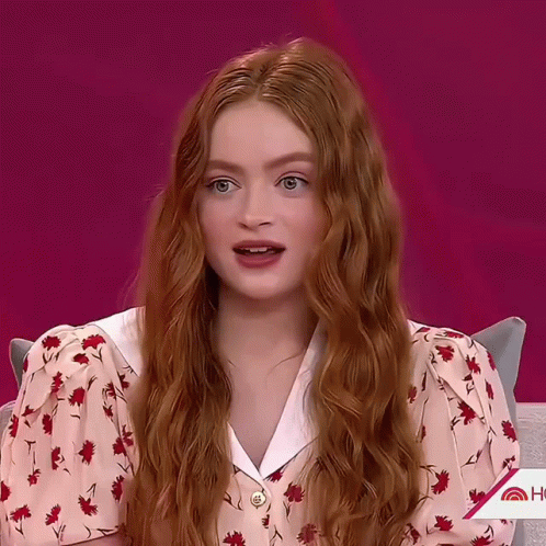 A Woman With Long Red Hair Is Wearing A Pink Floral Shirt GIF