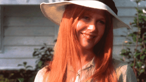 a woman with long red hair is wearing a white hat and smiling