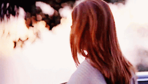 A Woman With Long Red Hair Looks At A Fire GIF