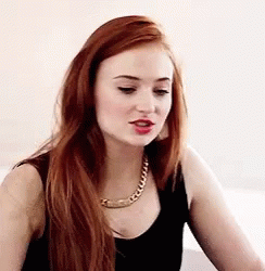 A Woman With Long Red Hair Wearing A Black Tank Top And A Gold Chain Necklace . GIF