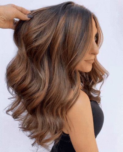 A Woman With Long Wavy Brown Hair Is Wearing A Black Top GIF