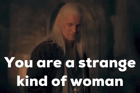 A Woman With Long White Hair Is Standing In A Dark Room With The Words `` You Are A Strange Kind Of Woman '' Above Her . GIF