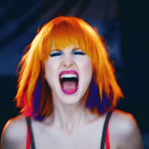A Woman With Orange And Purple Hair Is Screaming With Her Mouth Open GIF