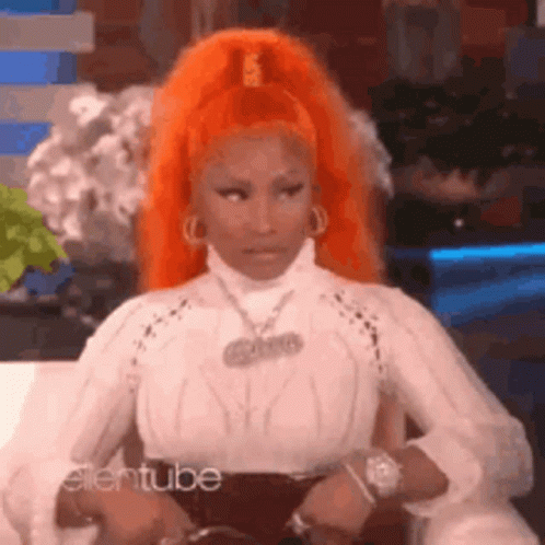 A Woman With Orange Hair Is Sitting On A Couch Wearing A White Shirt . GIF