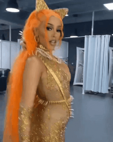 A Woman With Orange Hair Is Wearing A Gold Costume GIF