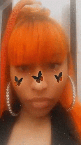 A Woman With Orange Hair Is Wearing Hoop Earrings And Has Three Butterflies On Her Face . GIF