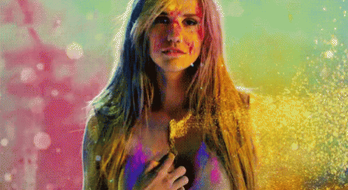 A Woman With Paint On Her Face Is Standing In Front Of A Pink And Blue Background GIF
