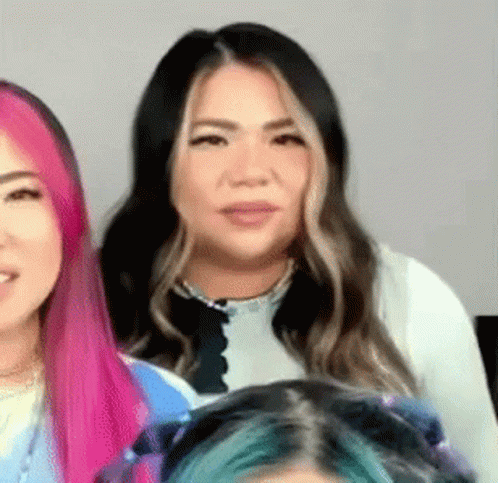 A Woman With Pink And Blue Hair Is Standing Next To Another Woman . GIF