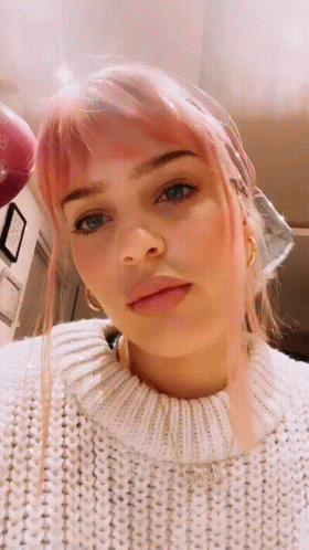 A Woman With Pink Hair And A White Sweater Looks At The Camera GIF
