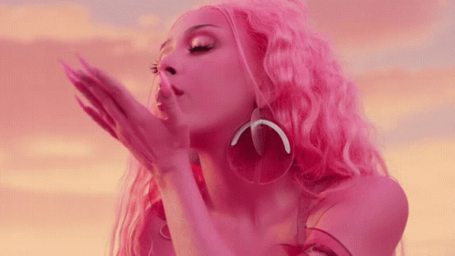 A Woman With Pink Hair And Earrings Blowing A Kiss GIF