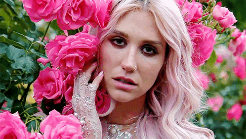 A Woman With Pink Hair And Gloves Is Surrounded By Pink Roses In A Garden . GIF
