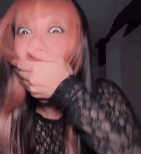 A Woman With Pink Hair Is Covering Her Mouth With Her Hand . GIF