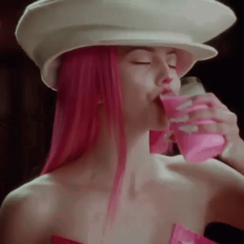 a woman with pink hair is drinking a pink drink from a can .