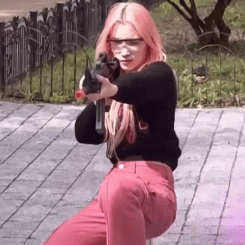 A Woman With Pink Hair Is Holding A Gun In Her Hand While Wearing Safety Glasses . GIF