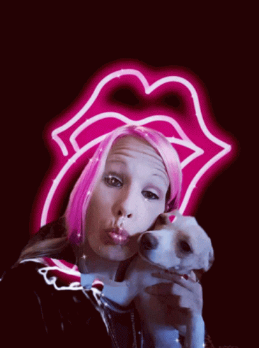 A Woman With Pink Hair Is Holding A Small Dog In Front Of A Neon Sign That Says Rolling Stones GIF