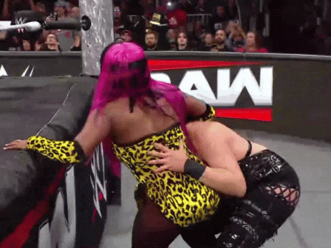 A Woman With Pink Hair Is Hugging Another Woman In Front Of A Raw Sign GIF