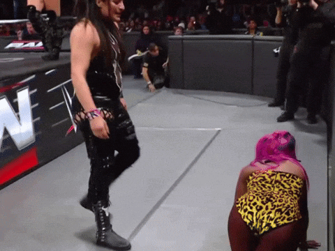 A Woman With Pink Hair Is Kneeling On The Ground In Front Of A Sign That Says N GIF