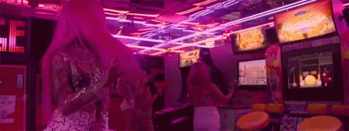 A Woman With Pink Hair Is Playing A Video Game In An Arcade With Neon Lights . GIF