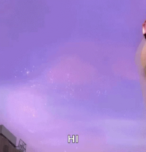 A Woman With Pink Hair Is Saying Hi In Front Of A Purple Background GIF