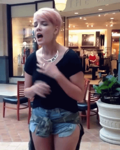 A Woman With Pink Hair Is Singing In Front Of A Store That Says ' The Loft ' On It GIF