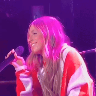 A Woman With Pink Hair Is Singing Into A Microphone On A Stage GIF
