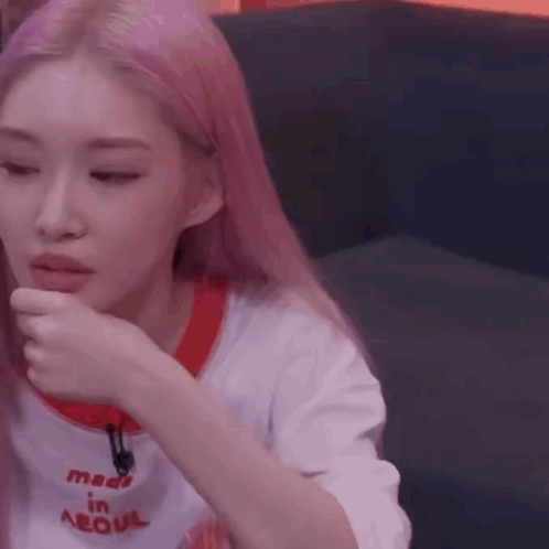 A Woman With Pink Hair Is Sitting On A Couch With Her Hand To Her Face . GIF