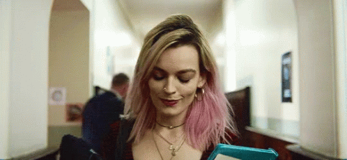 A Woman With Pink Hair Is Smiling And Looking Down GIF
