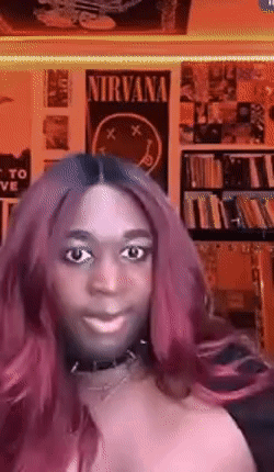 A Woman With Pink Hair Is Smiling In Front Of A Nirvana Poster On The Wall GIF
