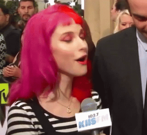 A Woman With Pink Hair Is Speaking Into A Microphone That Says 102.7 Kms Fm GIF