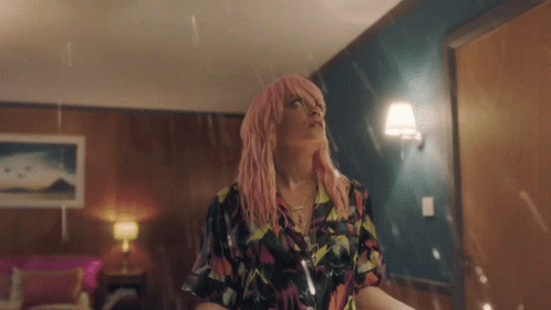 A Woman With Pink Hair Is Standing In A Room In The Rain GIF