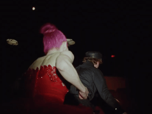 a woman with pink hair is standing next to a man in a black suit