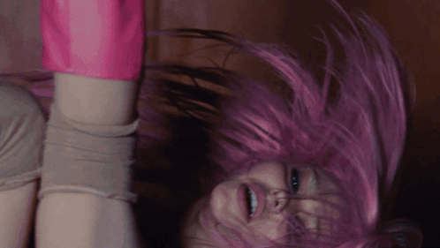 a woman with pink hair is upside down and smiling