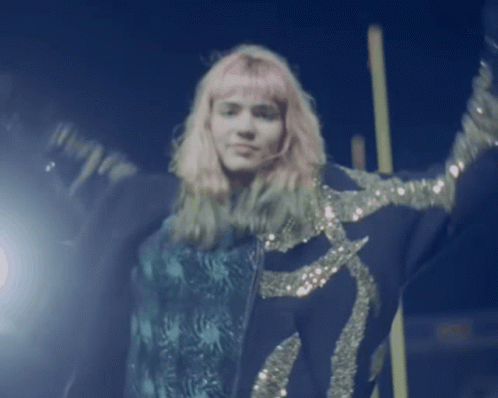 A Woman With Pink Hair Is Wearing A Blue Jacket With Sequins GIF