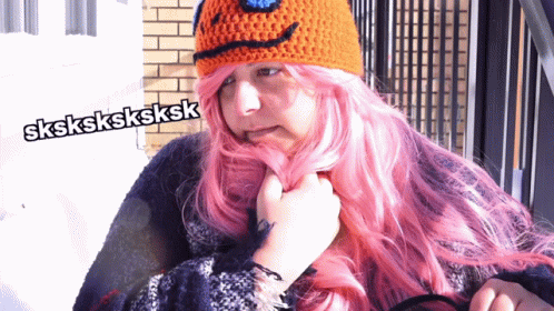 A Woman With Pink Hair Is Wearing An Orange Crocheted Hat GIF