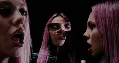 a woman with pink hair looks at herself in the mirror