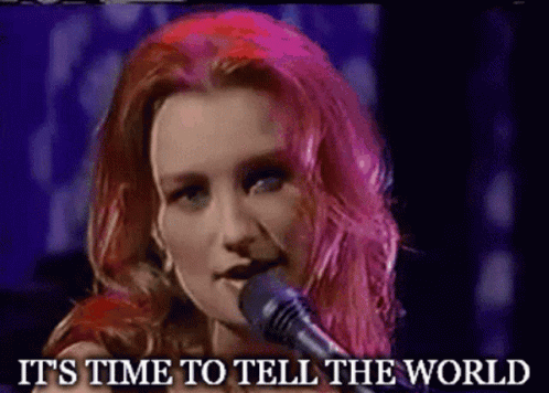 A Woman With Pink Hair Singing Into A Microphone With The Words " It 'S Time To Tell The World " Written Below Her GIF