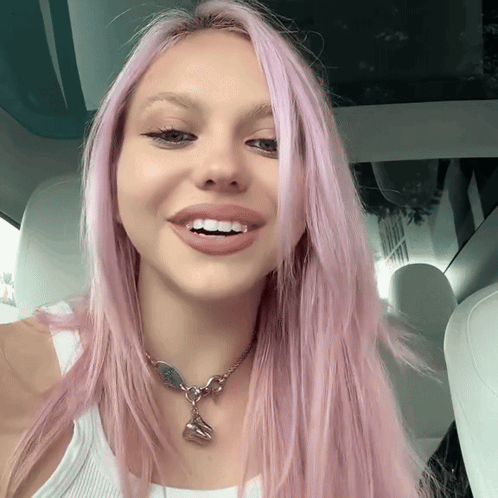 a woman with pink hair wearing a white tank top and a necklace