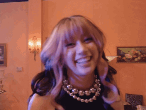 A Woman With Purple Hair And A Necklace Is Smiling GIF