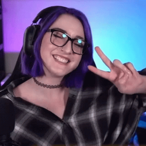A Woman With Purple Hair And Glasses Is Giving A Peace Sign While Wearing Headphones . GIF