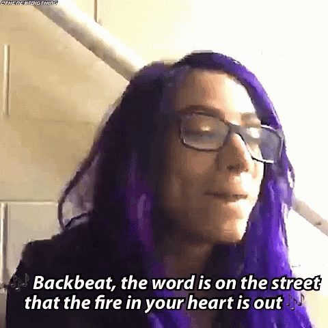 a woman with purple hair and glasses is wearing a purple wig .
