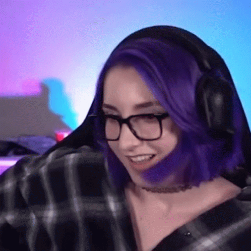 A Woman With Purple Hair And Glasses Is Wearing Headphones While Playing A Video Game . GIF