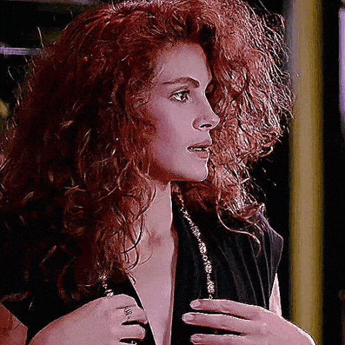 A Woman With Red Curly Hair Is Wearing A Black Shirt GIF