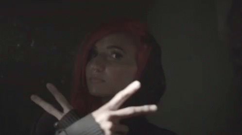 A Woman With Red Hair And A Black Hoodie Is Making A Peace Sign GIF
