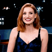 A Woman With Red Hair And A Blue Dress Is Smiling . GIF